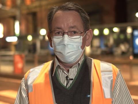 A head and shoulders shot of a middle-aged man wearing a face mask and hi vis vest looking directly at camera.