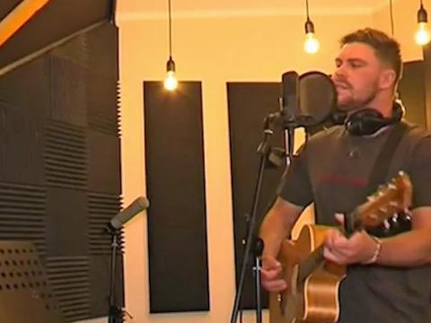 A young man in a recording studio holding a guitar and singing into a microphone.