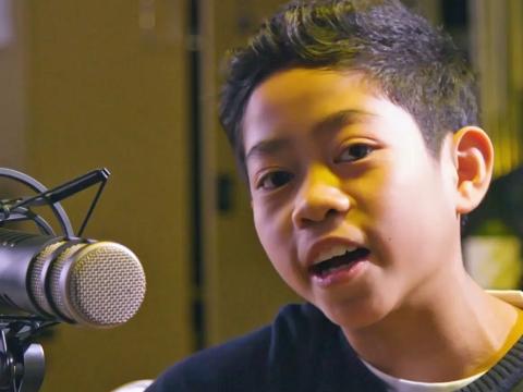 Close up of an 11-year-old Asian boy singing into a recording studio microphone.