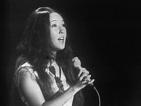 A teenage girl with long dark hair sings into a microphone