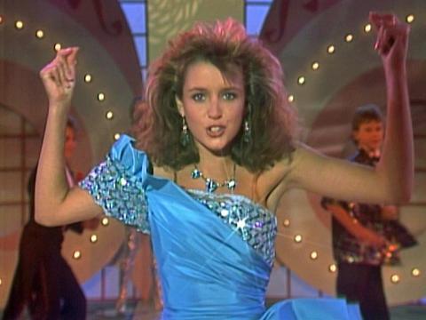 A teenage girl in a blue formal gown performing in a TV studio