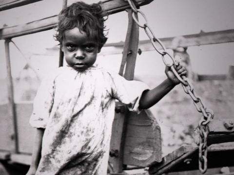 An Aboriginal child looking into camera holding a chain
