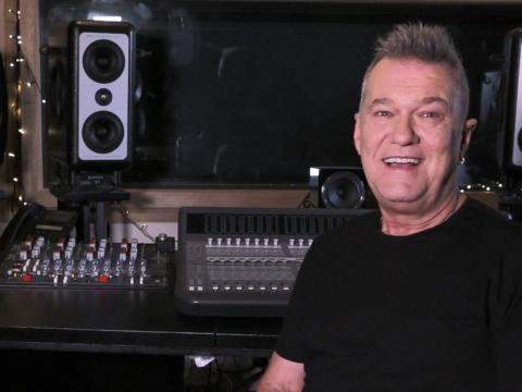 Singer Jimmy Barnes pictured from the chest up, in a black t-shirt and sitting in front of a mixing deck in a recording studio. 