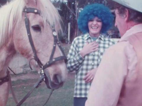Jeanne Little is laughing, standing next to Smoky Dawson's horse Flash. She is dressed in a blue wig.