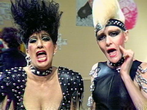 Maria Venuti and Jeanne Little dressed up in leather and chains with punk hairstyles. They are singing to camera.