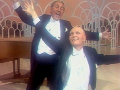 Jeanne Little in drag and John-Michael Howson - both wearing tuxedos with their arms outstretched.