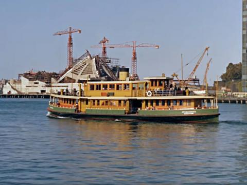 Sydney Harbour and Circular Quay, with a ferry passing in front of the Sydney Opera House, still under construction.