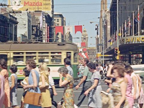 A busy street in Melbourne city with pedestrians and a tram going past.