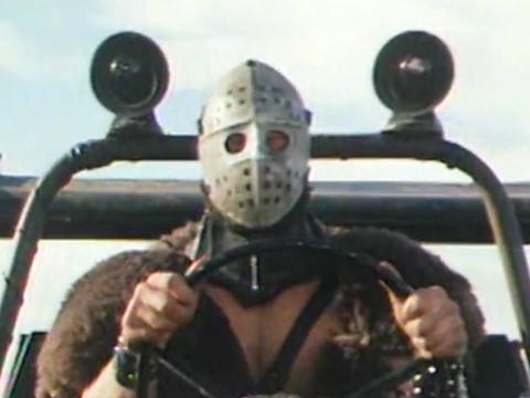 A man in a hockey mask drives a buggy down the highway in Mad Max 2