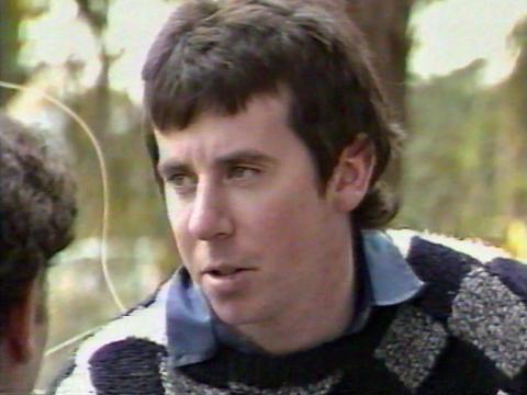 Head and shoulders shot of a young man with dark hair looking away from camera. He is wearing a checked jumper and collared shirt.