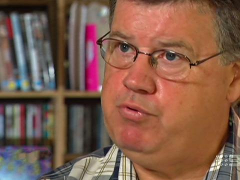 Close up of a middle aged man's face with bookshelves in the background. 
