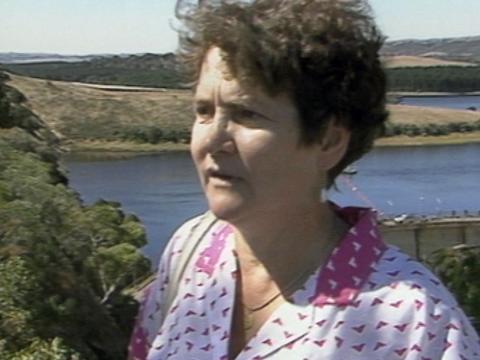 Head and shoulders shot of a woman with short hair and pink top standing in front of a large body of water.