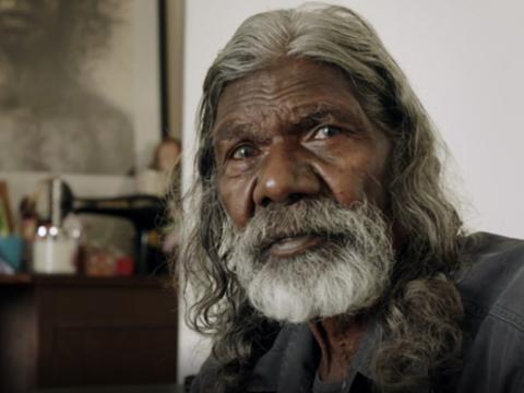 Actor David Gulpilil is looking at the camera with a sombre expression.