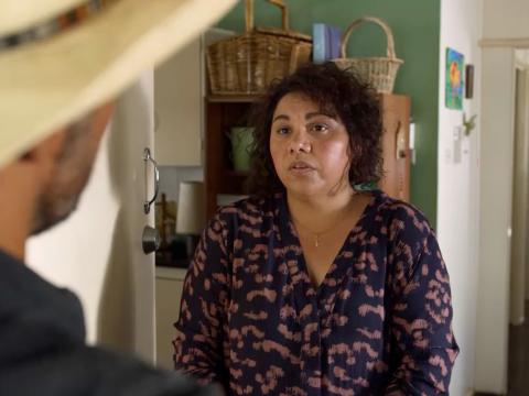 A woman standing at an open door looking at a man in a hat on the other side who we can only see the back of.