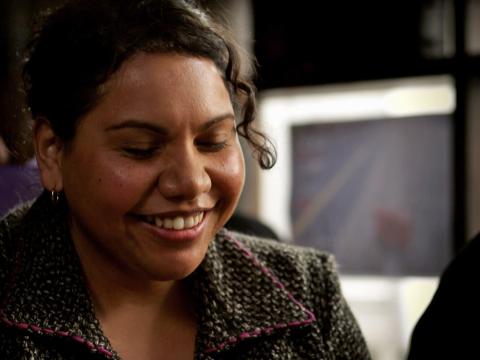 Close up of actor Deborah Mailman looking downwards with a smile on her face.