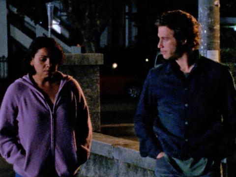 A young woman and man walking together at night, side by side. Both are looking very solemn