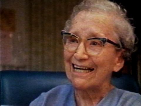 An elderly woman wearing glasses smiling