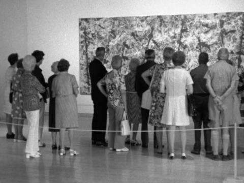A group of people with their backs to the camera in the Art Gallery of NSW look at Jackson Pollock's artwork 'Blue Poles'