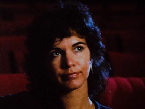 Artist Tracey Moffatt looks up towards a film being projected in an empty movie theatre with red seats.