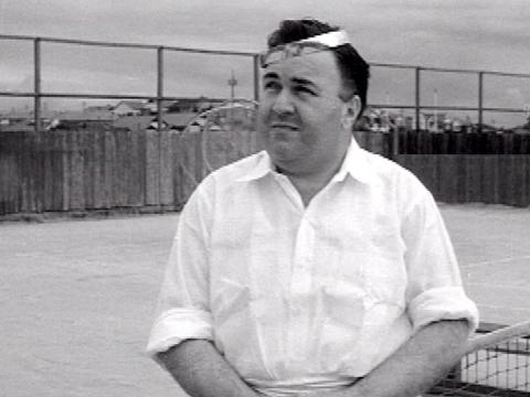 A man dressed as cupid with a halo and wings made of wire. He's wearing tennis whites and is at a tennis court.