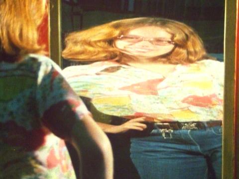 A woman looks at her distorted reflection in a mirror