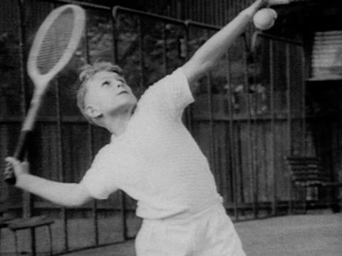 A young boy serves a tennis ball