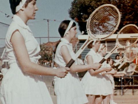A row of young girls lined up practising tennis strokes.