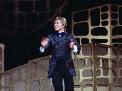 John Farnham pictured on stage circa 1970, wearing a long double-breasted pinstripe jacket and bowtie.