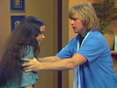 Sigrid Thornton and John Farnham in a scene from the TV sitcom Bobby Dazzler (1977). They are standing in a living room and Farnham is holding Thornton by the shoulders looking at directly at her with a confused expression.