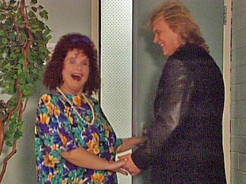 Pixie Anne Wheatley (Magda Szubanski) from Fast Forward holding hands with John Farnham and smiling back at the camera.