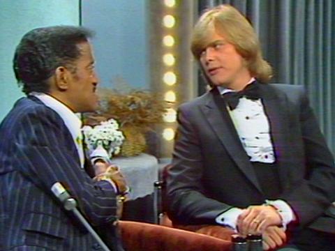 Sammy Davis Jr and John Farnham seated, talking to one another on the set of the The Don Lane Show. 