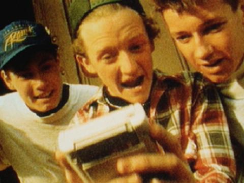 Three teenagers crowd around while one players a Nintendo Game Boy