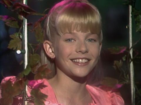 Rikki Arnot smiles for the camera. She is wearing a pink dress and and her teeth and her blonde hair shine brightly.
