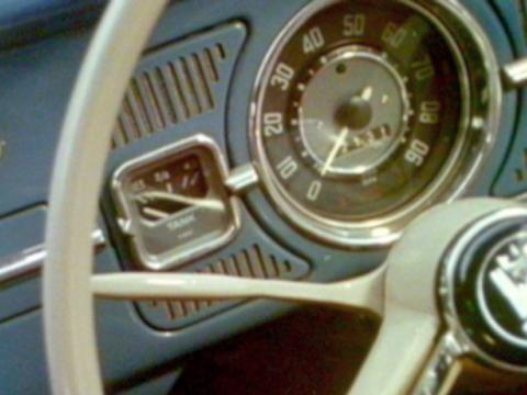 We see the white steering wheel and the speedometer of a vintage car. 