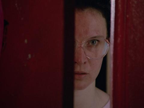 Close up of Fran in the film Strictly Ballroom, played by Tara Morice, peeks through a doorway of a dance studio.