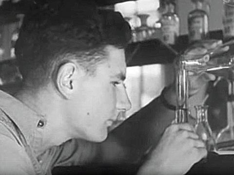 Close up of a young man at the University of Western Australia watching closely as he pours a liquid from a glass beaker into a thin test tube. 