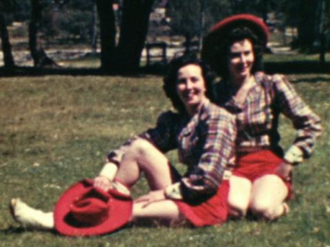 Two girls sitting on the grass wearing matching cowgirl outfits.