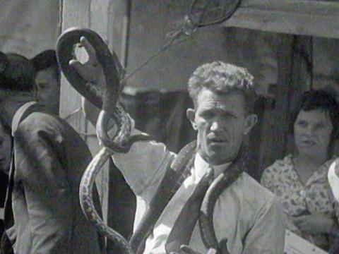 A man holds up a snake with people looking on.