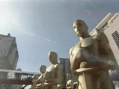 Giant Oscar statuettes stand in the sunshine outside a building.