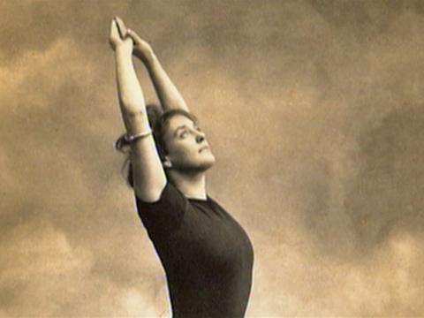 Annette Kellerman as a young woman strikes a pose with her arms above her head. She is dressed in a short-sleeved swimming costume.