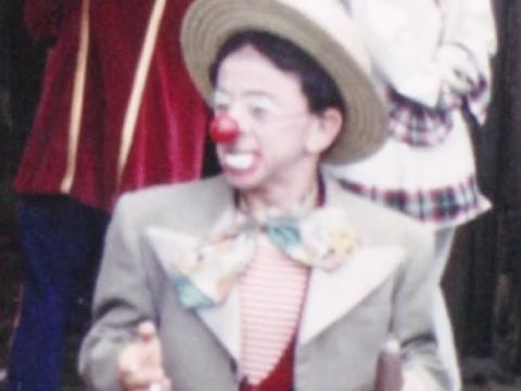 A clown wearing a hat, suit with a red nose.