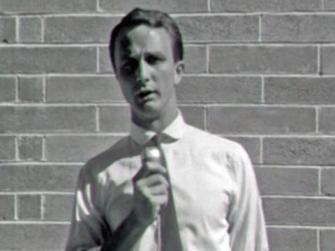 Frame capture of a news reporter with a microphone speaking to camera