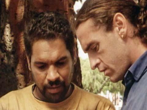 Two men in a park lean towards each other, talking