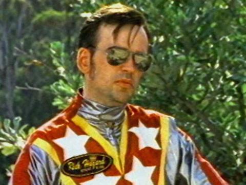 Man wearing sunglasses and dressed like a motorcycle stunt person.