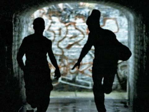 The silhouetted figures of two young men running through a graffitied tunnel
