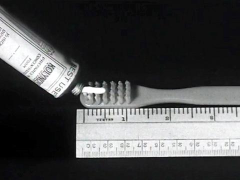 Shot from a commercial of a toothbrush sitting next to a ruler and some toothpaste being squeezed onto the toothbrush bristles.