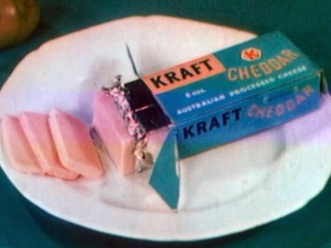 A block of Kraft cheese sitting on a white dinner plate. The cheese packaging is open and a few slices of the cheese have been sliced off.