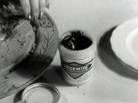 A jar of vegemite sitting on a table next to a dinner plate.
