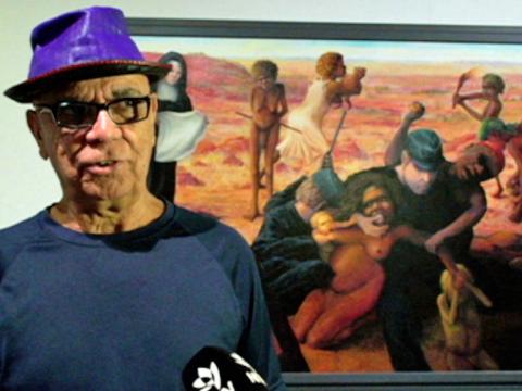 Artist Harold Thomas stands in front of one of his artworks 'Tribal Abduction' depicting the removal of Aboriginal children from their country and their families.