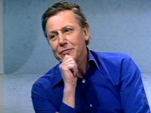 David Attenborough in a thinking pose while he is being interviewed. He's wearing a bright blue shirt.